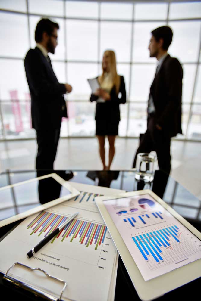 Financial reports on a conference table with professionals meeting in the background, showcasing expert business financial consultant Fort Lauderdale services