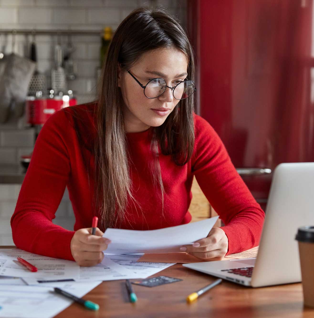Woman reviewing financial documents at a desk with a laptop, calculator, and paperwork, focused on budgeting and filing taxes at home, Tax Preparation Miami